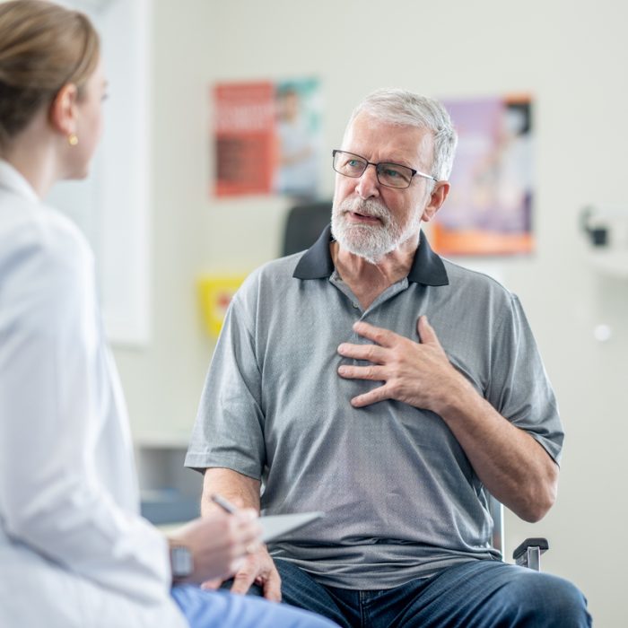 A senior gentleman of sits with his female doctor during a medical appointment. He is dressed casually as he talks with his doctor who is seated in front of him and taking notes on a tablet.