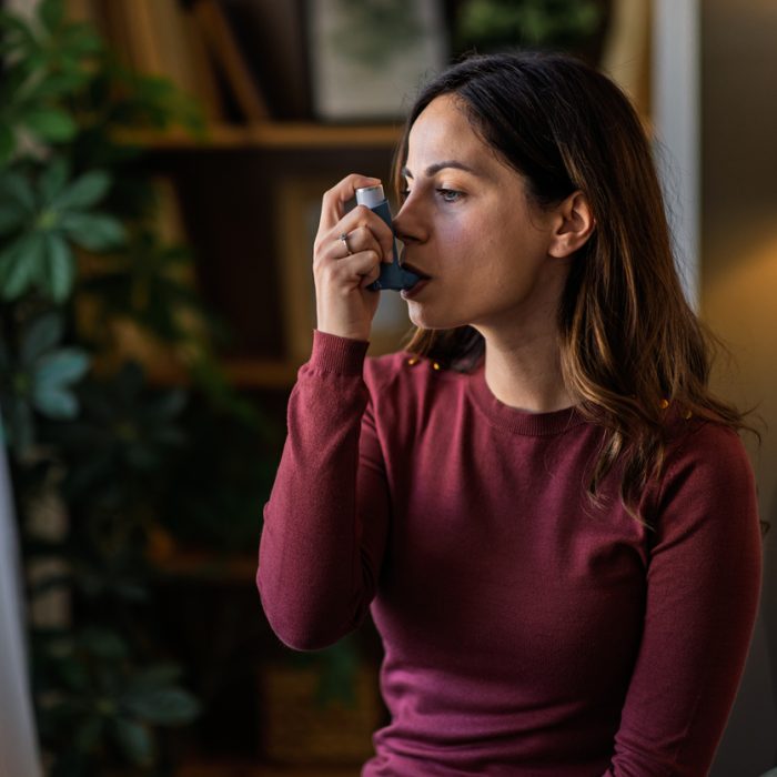 Young woman using her asthma inhaler at home