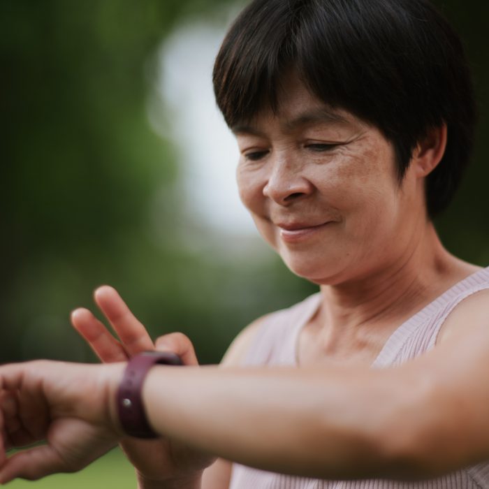 Asian mature woman using fitness tracking app while exercising in the park.