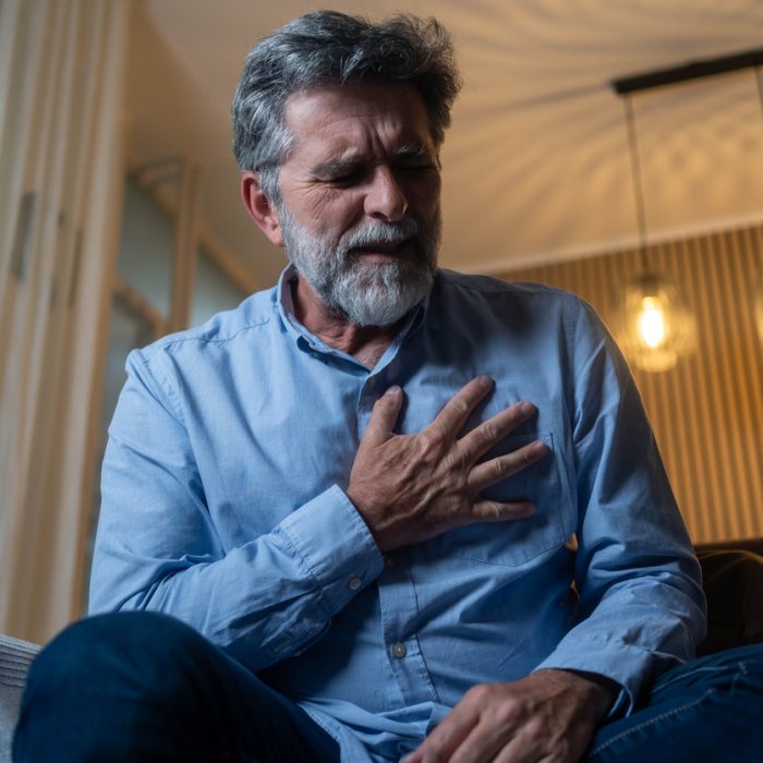 Mature man having a chest pain while sitting in living room at home.