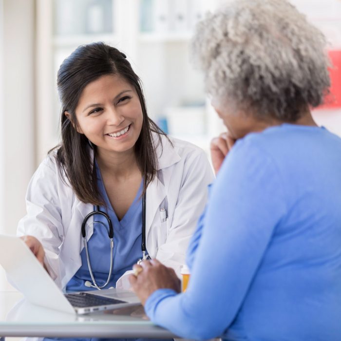 Young nurse uses laptop while sitting with senior patient