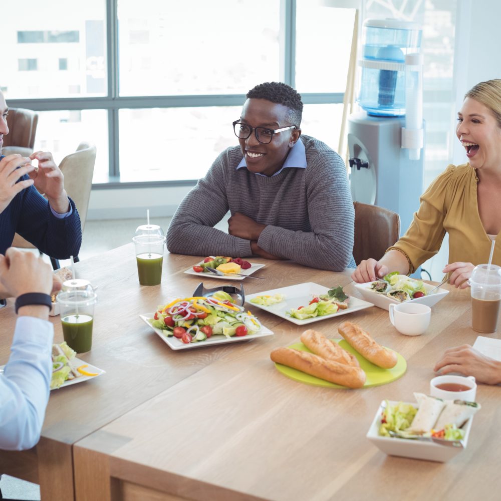Happy business colleagues having lunch on table at office cafeteria