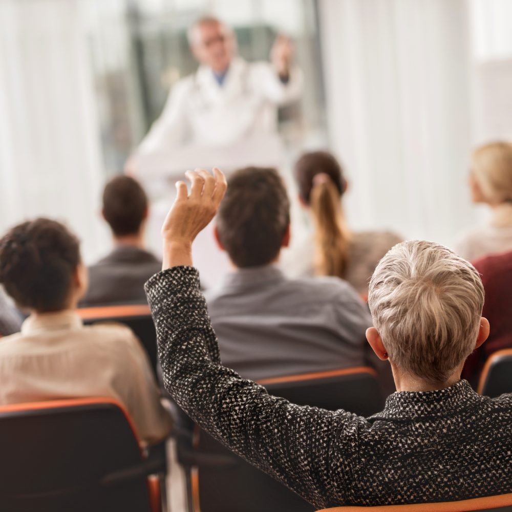 Back view of a woman raising her hand ready to ask a question on education seminar about medicine.