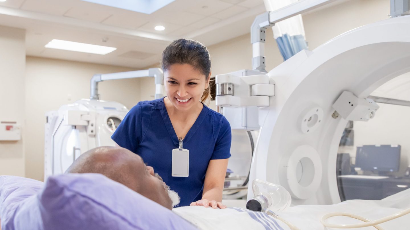 Female nurse prepares senior male for treatment in hyperbaric chamber