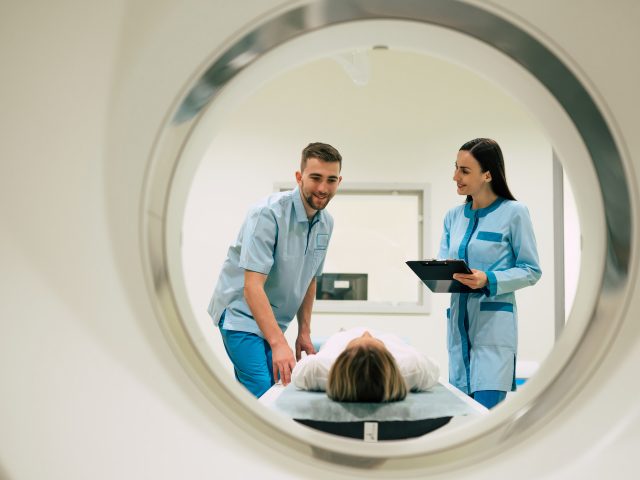 Professional Doctor Radiologist In Medical Laboratory Controls magnetic resonance imaging or computed tomography or PET Scan with Female Patient Undergoing Procedure.