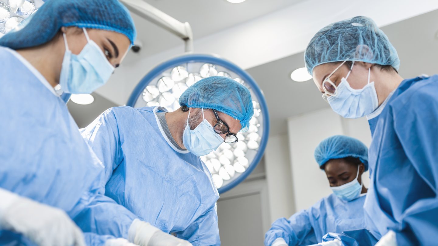Diverse Team of Professional surgeon, Assistants and Nurses Performing Invasive Surgery on a Patient in the Hospital Operating Room. Surgeons Talk and Use Instruments. Real Modern Hospital.