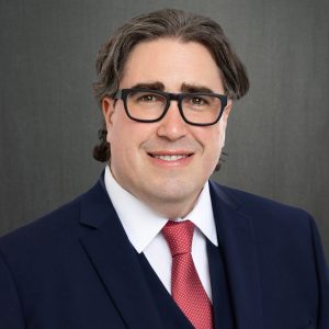 man wearing glasses and navy suit and red tie