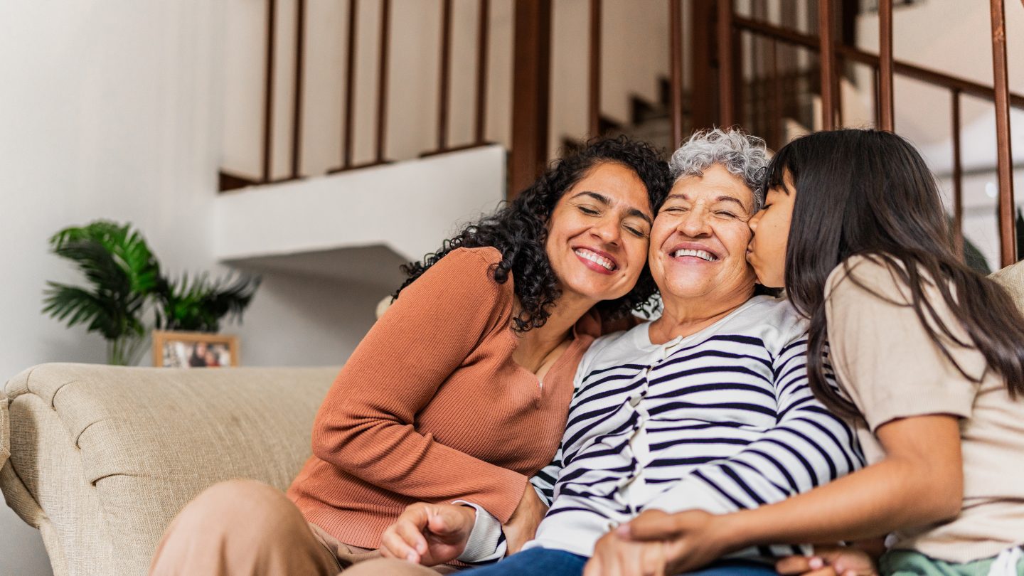 Senior woman receiving kisses from daughter and granddaughter at home