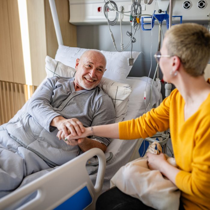 Senior man receiving support from his daughter during recovery in a hospital room